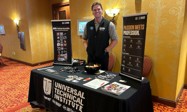 Universal Technical Institute Exhibitor standing behind a table