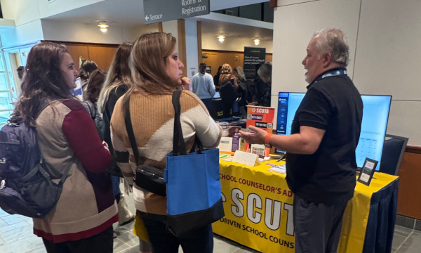 Conference attendees speaking with an exhibitor about school counseling resources.
