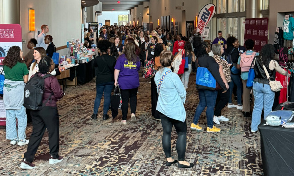 School counselors exploring exhibitor booths and networking in a crowded conference exhibit hall.