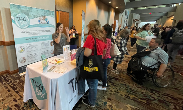 School counselors talking with an exhibitor at a booth featuring classroom resources during the conference exhibit hall.