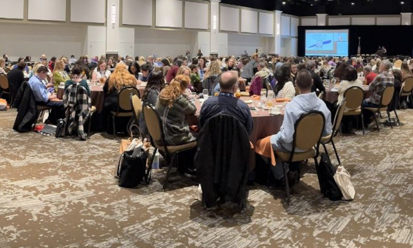 Large seminar room with attendees facing a presentation on a main screen
