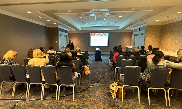 View of a breakout session room filled with chairs and people sitting, a podium, and a screen