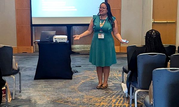 A speaker in a teal dress speaking to people in chairs