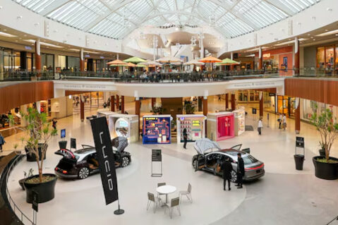 Interior picture of a mall with 2 stories, a car on the showroom floor, and stores on both sides