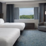 A guest room with two queen beds, a window, desk, and chair