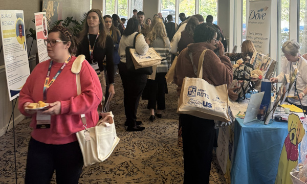 PSSCA Conference hallway with attendees walking past exhibitor tables, branded tote bags, informational booths, and promotional materials at a professional education event.
