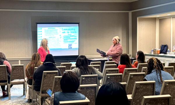 Presenters speaking to a seated audience in a classroom-style training session, with a projection board in the background