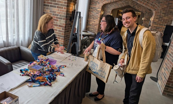 Conference registration area with attendees checking in at a table displaying name badges and event materials.