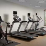 Hotel fitness center featuring treadmills, a stationary bike, an elliptical machine, and large windows providing natural light.